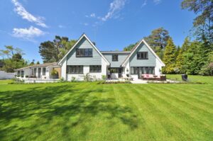 Extérieur d'une maison familiale moderne présentant une grande pelouse et un jardin sous un ciel bleu clair.