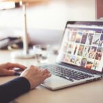 Gros plan de mains tapant sur un ordinateur portable avec une galerie d'images ouverte sur l'écran.